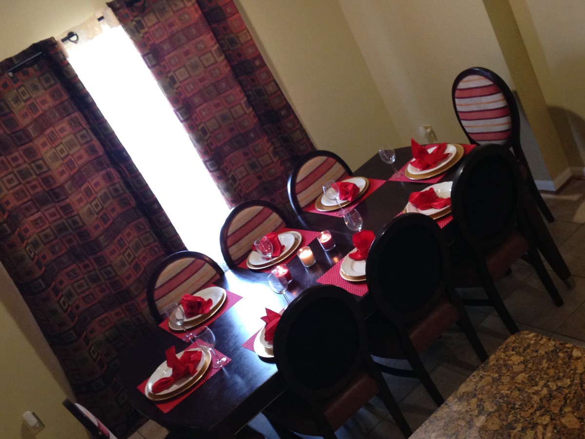 A dining room with a table set for guests, featuring red accents and striped chairs.