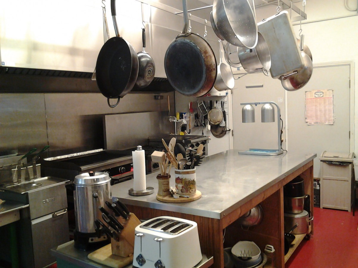 An industrial kitchen setup with hanging pots, a toaster, and a coffee maker on the countertop.