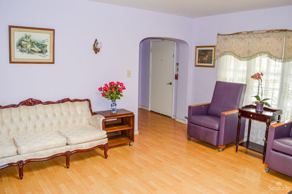 A cozy living room with a vintage couch and armchair, featuring a wooden floor and decorative flowers on a side table.