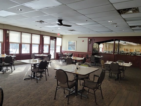 An empty dining room with several tables and chairs, well-lit by large windows.