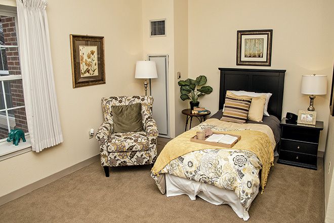 A cozy bedroom with a single bed, floral armchair, and decorative elements.