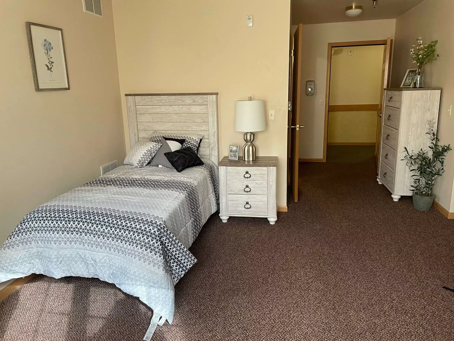 A cozy bedroom with a single bed, nightstand, and dresser in a neatly arranged space.