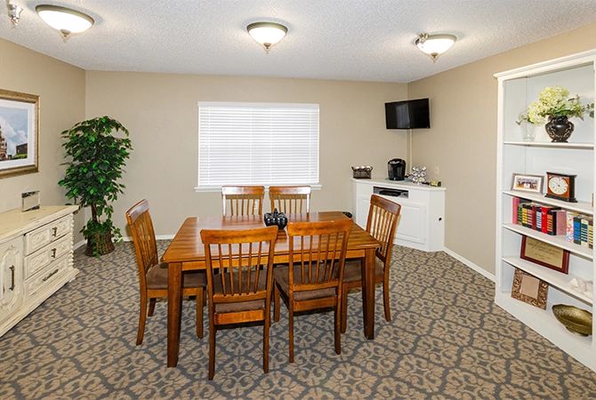 A cozy dining room featuring a wooden table and chairs, carpeted flooring, and a wall-mounted TV.