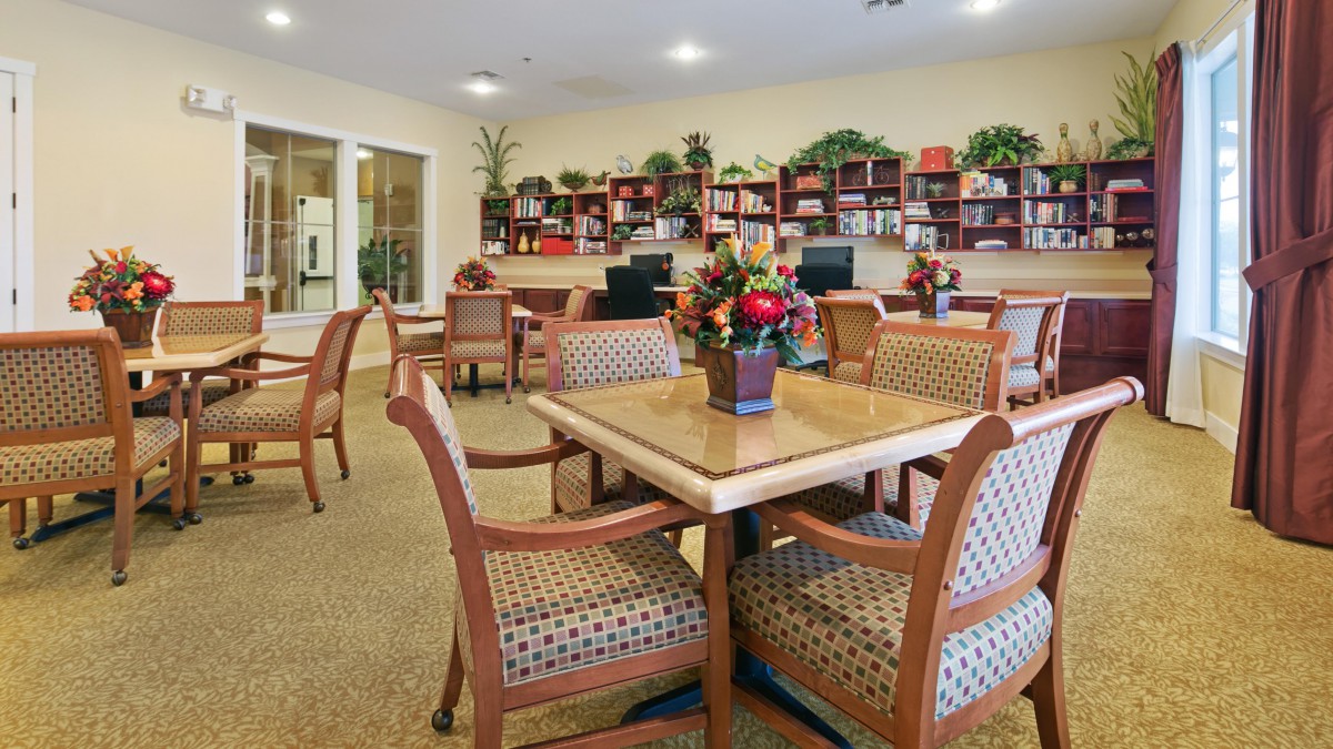 A comfortable community library setting with tables, chairs, and bookshelves filled with books.