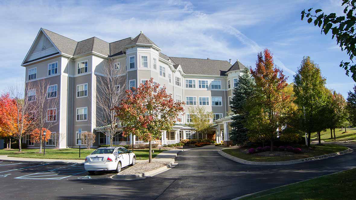 A residential building surrounded by trees with autumn foliage and a parked car in front.
