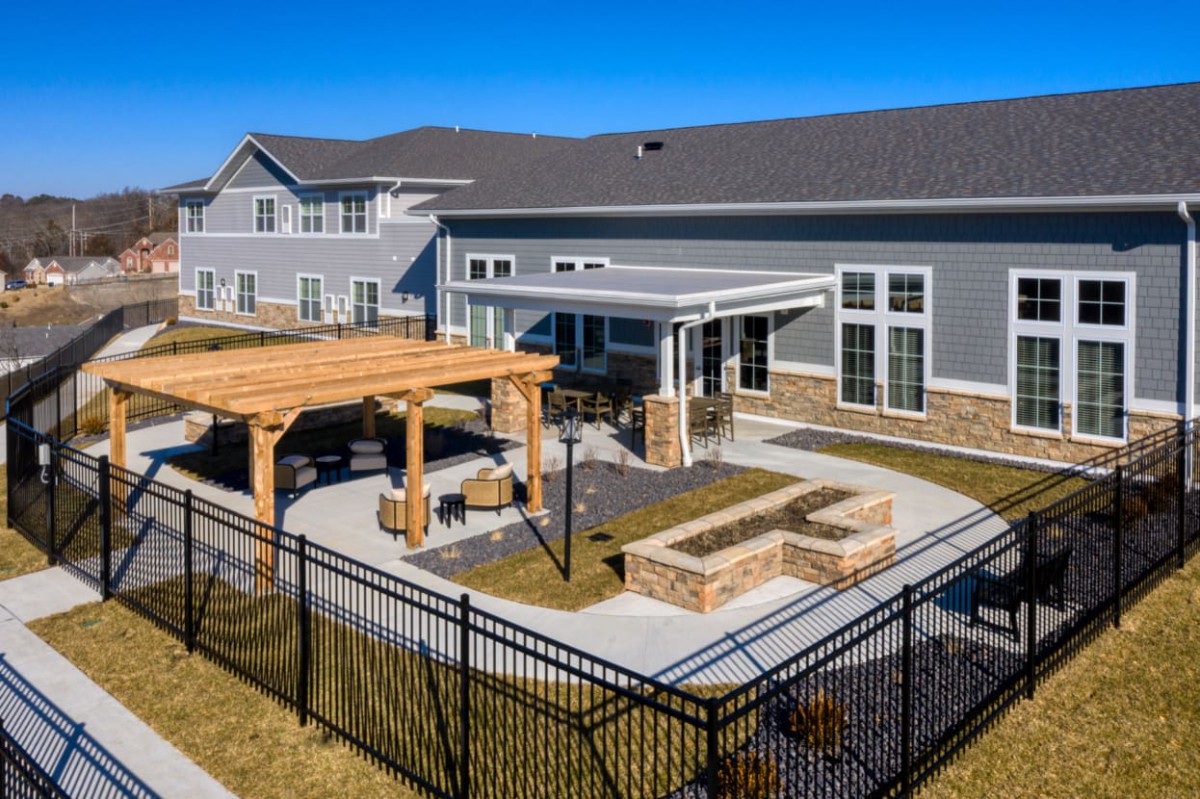 A modern residential building features a spacious backyard with a pavilion, patio, and fire pit under sunny skies.