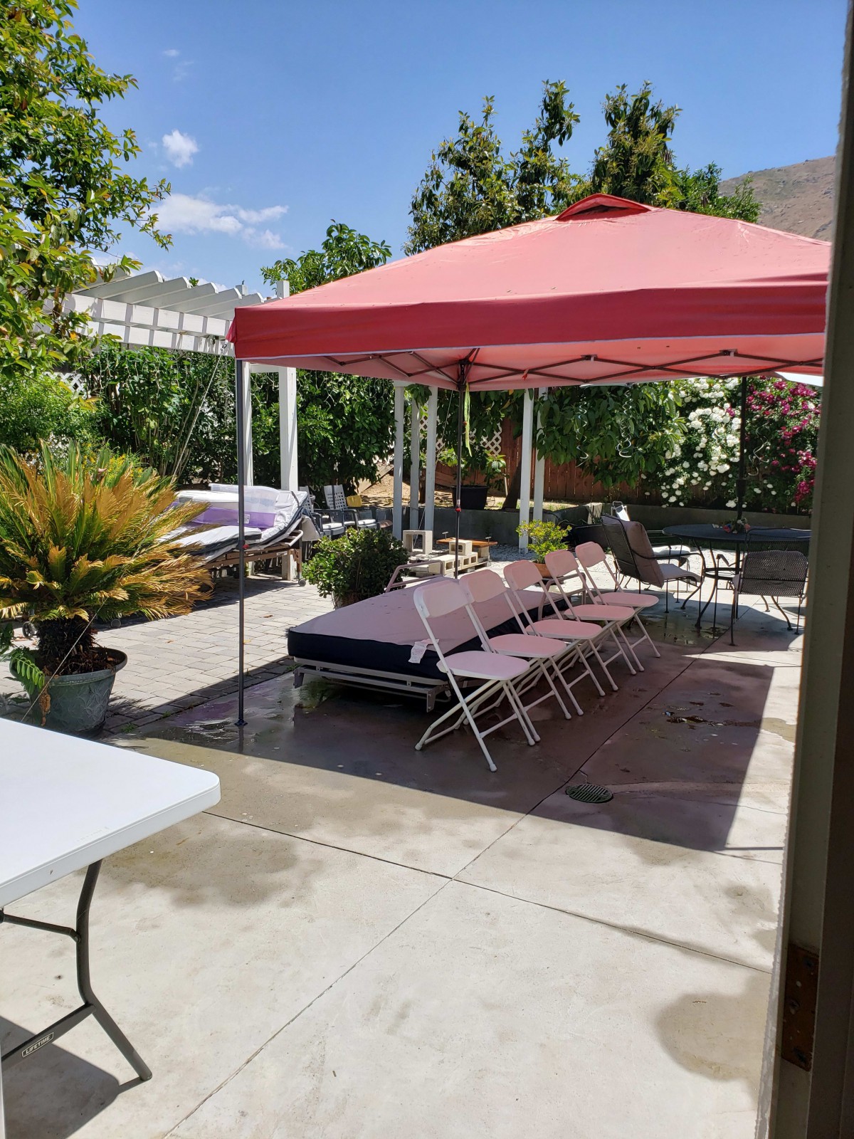 An outdoor patio set up with tables and chairs under a red canopy, ready for a gathering on a sunny day.