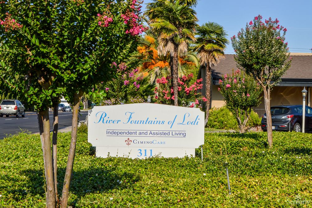 An outdoor sign for 'Rose Fountain of Life' surrounded by trees and landscaping.