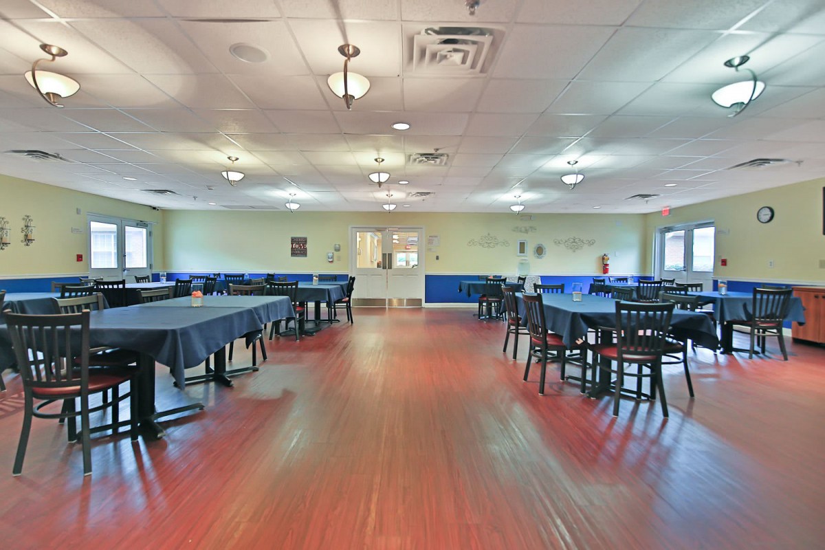 A spacious dining area with neatly arranged tables and chairs, featuring a wooden floor and soft lighting.