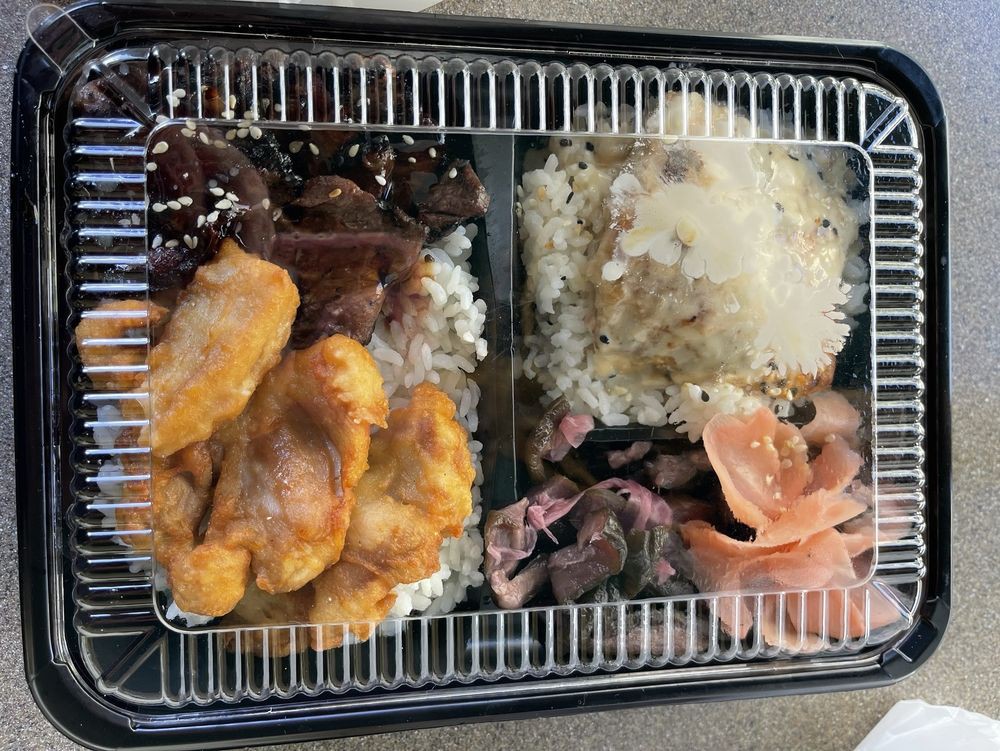 A bento box featuring rice, grilled beef, and fried chicken.
