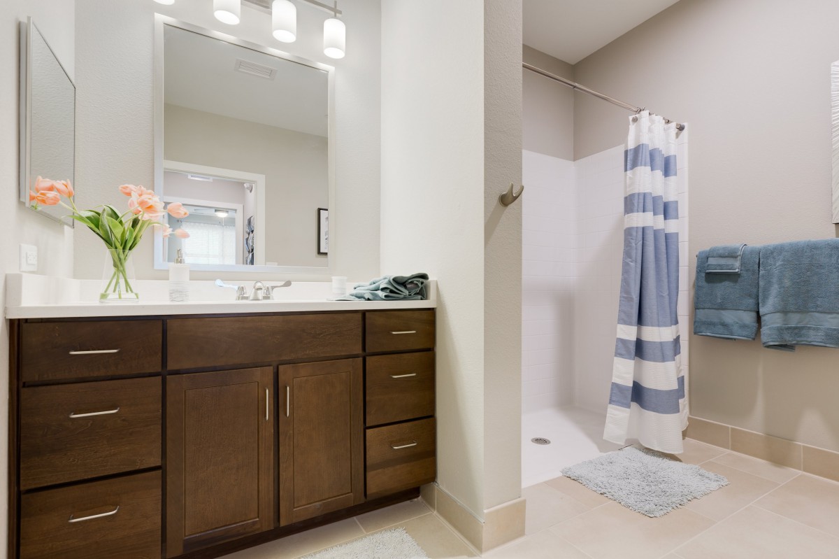 A modern bathroom with a wooden vanity, mirror, and a shower with a blue-striped curtain.