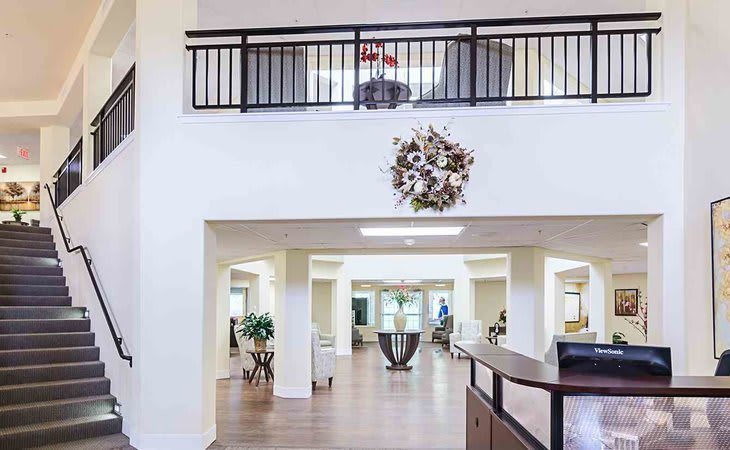 A modern lobby area with a reception desk, decorative wreath, and balcony.