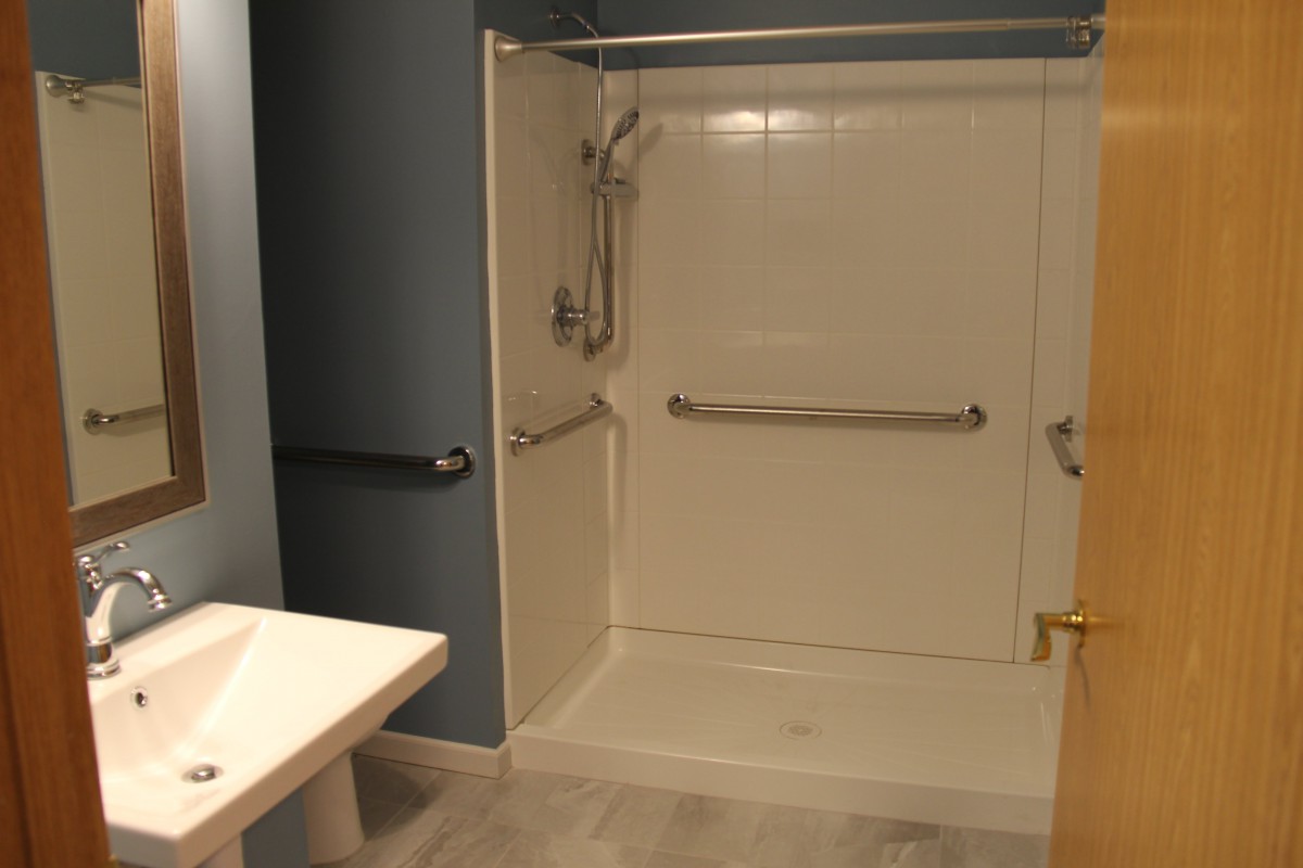 An accessible bathroom with a shower equipped with grab bars and a handheld showerhead, alongside a sink and tub seat.
