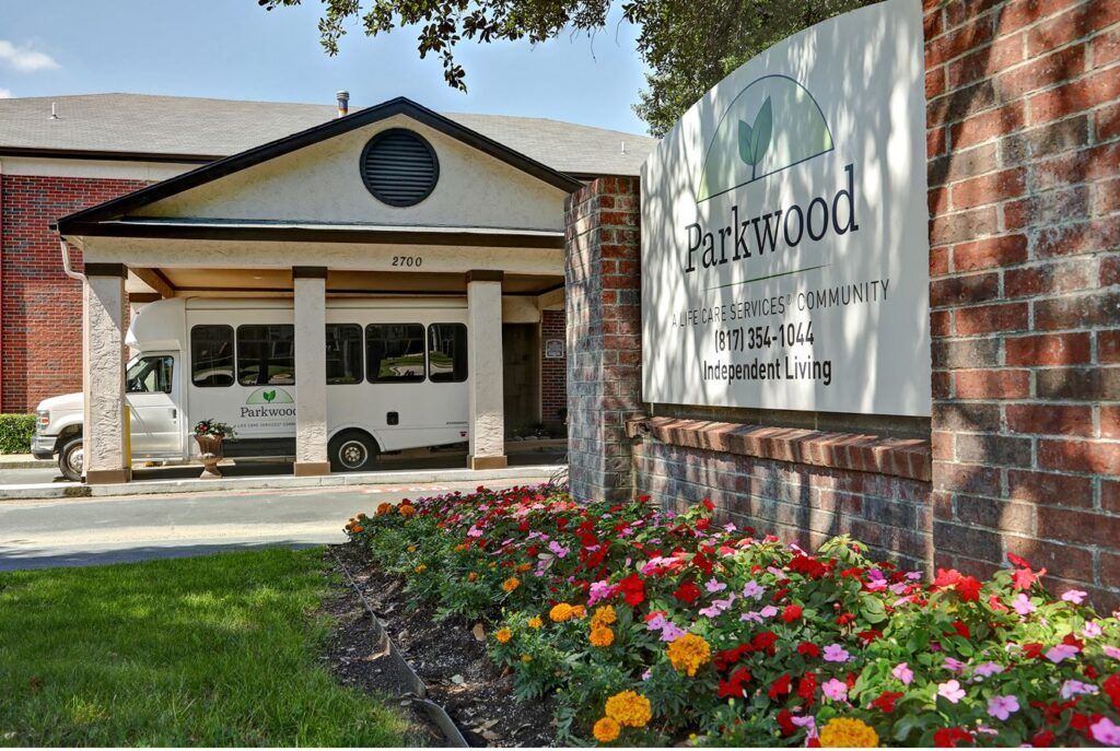 Entrance to a facility with a sign and colorful flowers in the foreground.