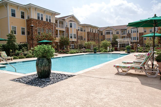 A residential apartment complex featuring an inviting outdoor swimming pool, surrounded by landscaped gardens and sun loungers.