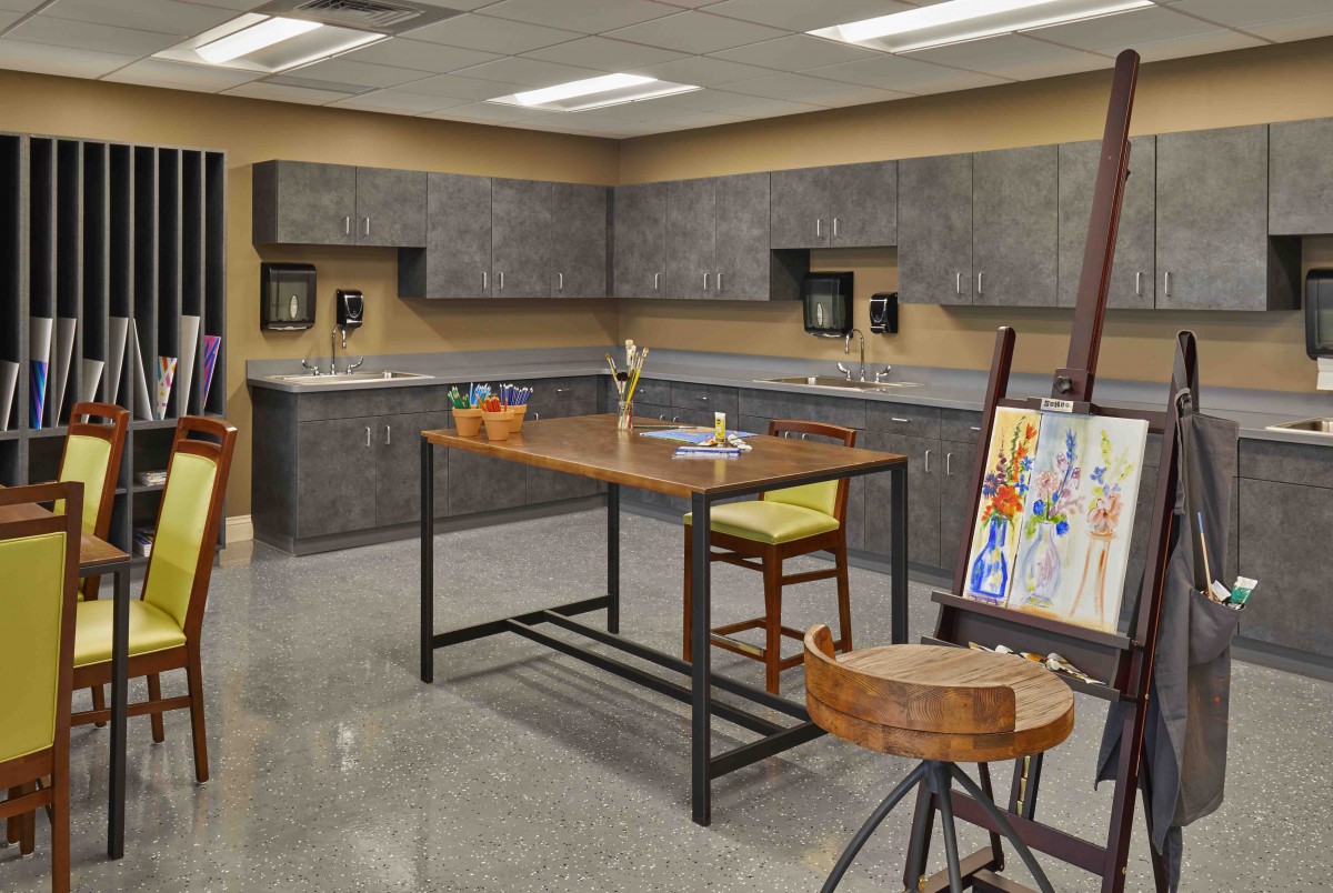 A well-equipped art studio featuring work tables, seating, and painting supplies.