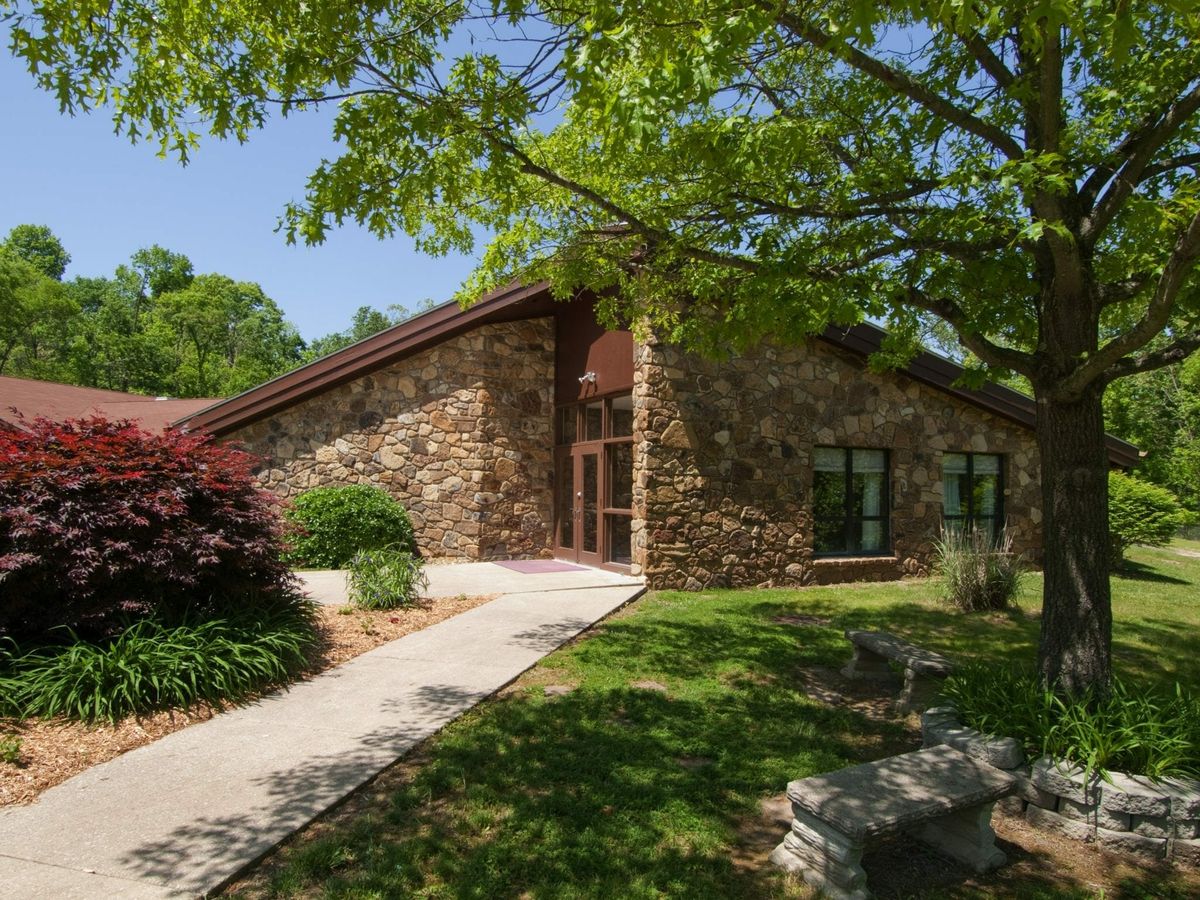 A stone building surrounded by lush greenery and trees on a sunny day.