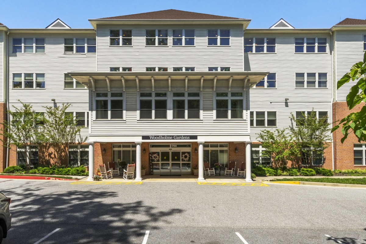 Front view of a multi-story residential building with a prominent entrance and parking area.