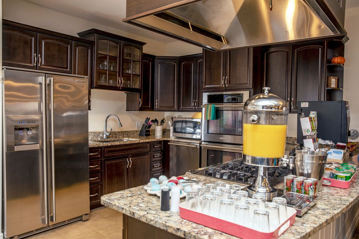 A modern kitchen featuring dark cabinets, stainless steel appliances, and a granite countertop with a juice dispenser.