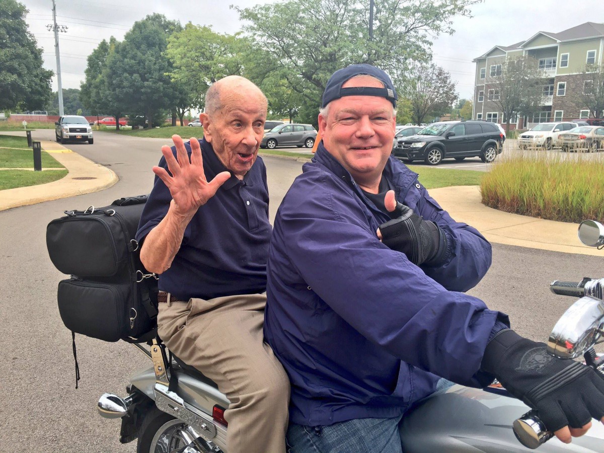 Two men enjoying a motorcycle ride together, smiling and waving.