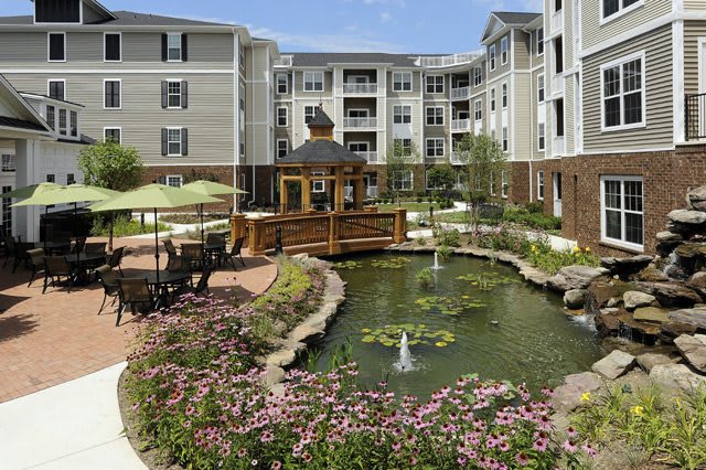 A beautifully landscaped apartment courtyard featuring a pond with fountains, surrounded by flowers and outdoor seating.
