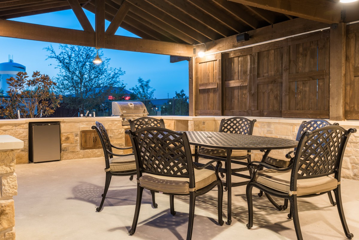 A cozy outdoor patio with a table and chairs under a covered structure, beautifully lit in the evening.
