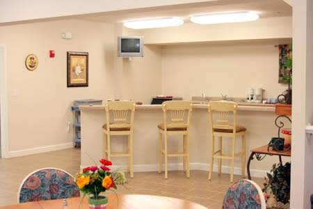A cozy interior with a bar area, featuring wooden stools, a small TV, and a table with vibrant flowers.
