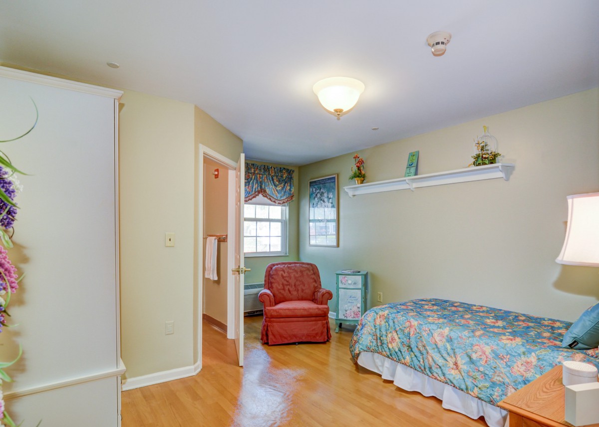 A bright bedroom with a single bed, armchair, and wooden flooring.