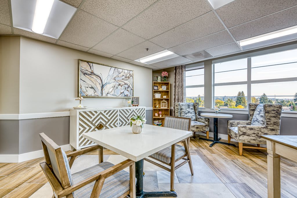 A modern office space featuring a table and chairs, wall art, and natural lighting from large windows.