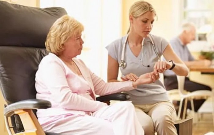 A nurse checking the pulse of an elderly patient during a medical visit.