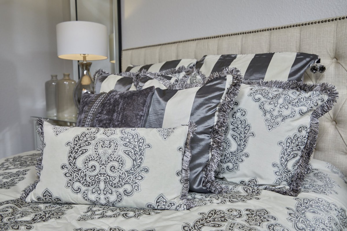 A cozy bed with decorative pillows and elegant bedding, complemented by a stylish lampshade.
