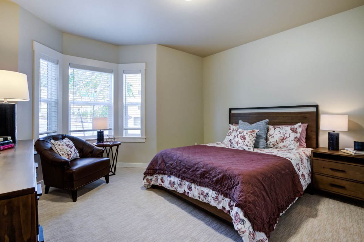 A cozy bedroom with a bed, armchair, and large windows.