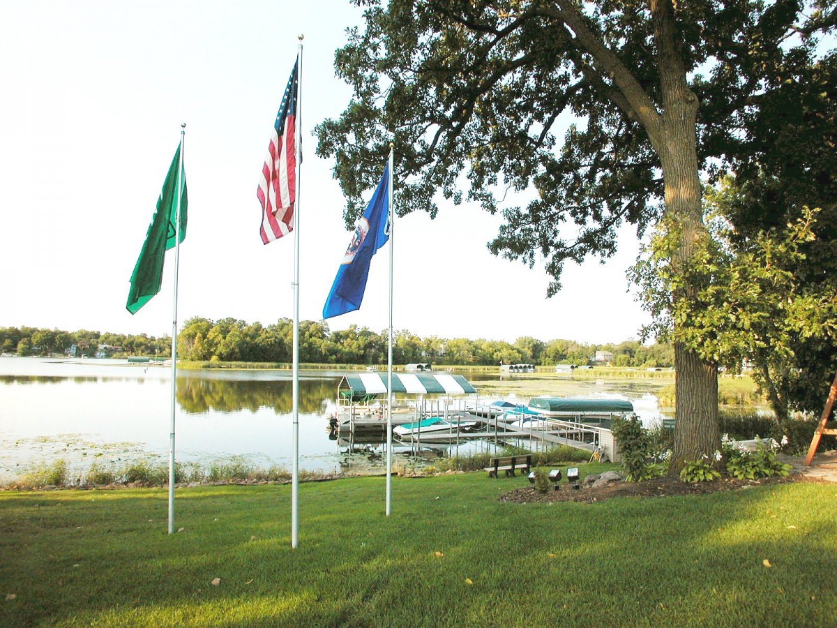 A scenic view of a lakeside dock with boats, surrounded by flags and trees.