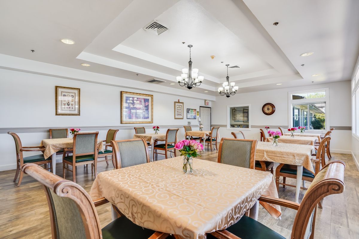 A spacious dining room with elegantly arranged tables and chairs, adorned with chandeliers and artwork on the walls.