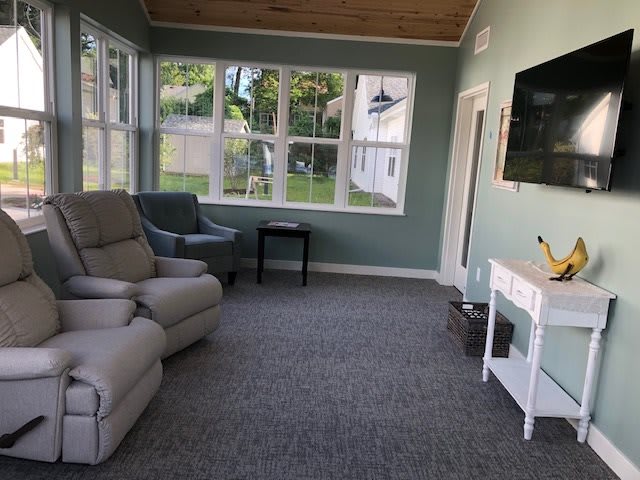 A cozy living room with large windows, comfortable seating, and a mounted TV.