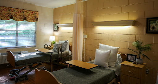 A well-lit patient room featuring two hospital beds with comfortable bedding.