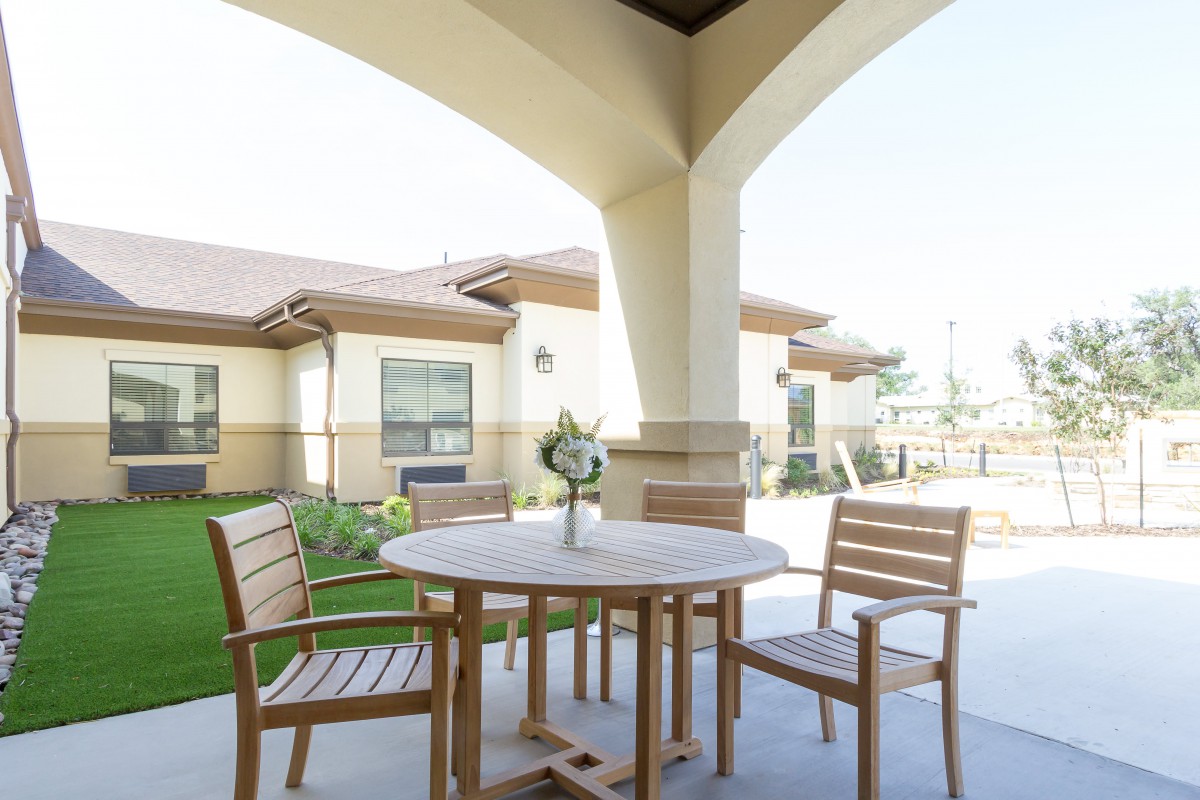 A sunny patio with wooden table and chairs in a garden setting.