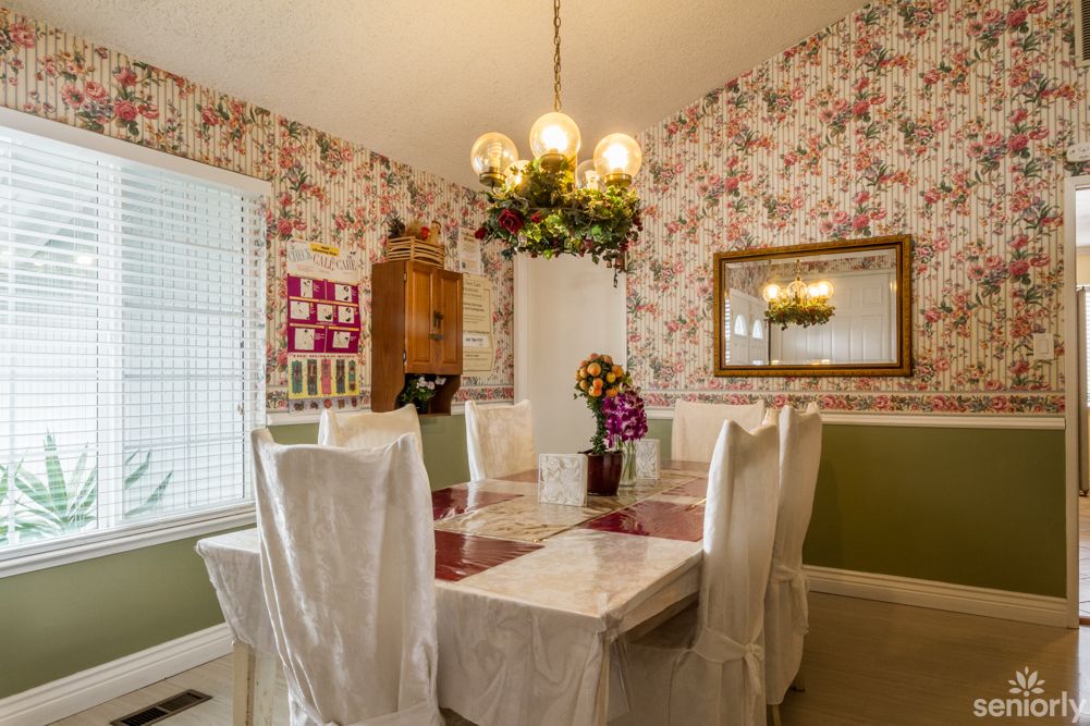 A cozy dining room with floral wallpaper, a chandelier, and a mirrored wall.