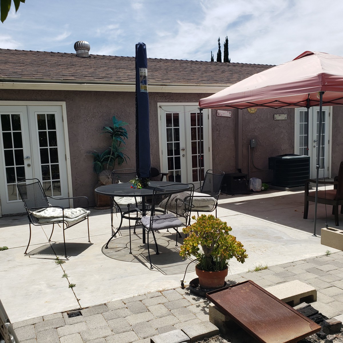 A sunny backyard patio with outdoor furniture and a pink canopy.