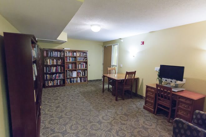 A cozy library room featuring bookshelves, a reading desk, and a computer station.