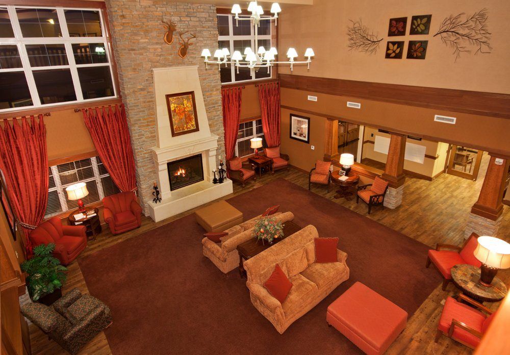 A cozy hotel lobby with a central fireplace, chandelier, and comfortable seating area adorned in warm colors.