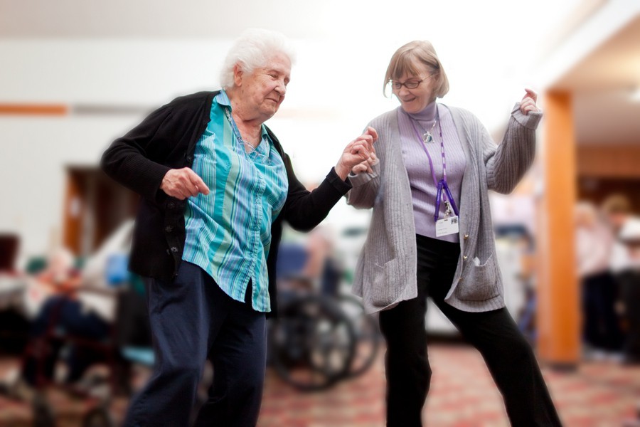 Two elderly women enjoying a dance together indoors.