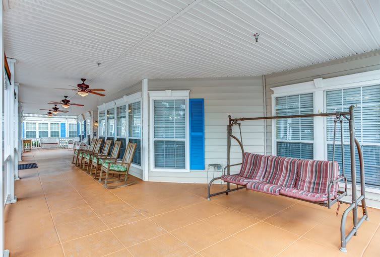 A spacious porch featuring a swing, multiple rocking chairs, and ceiling fans for a relaxing outdoor experience.