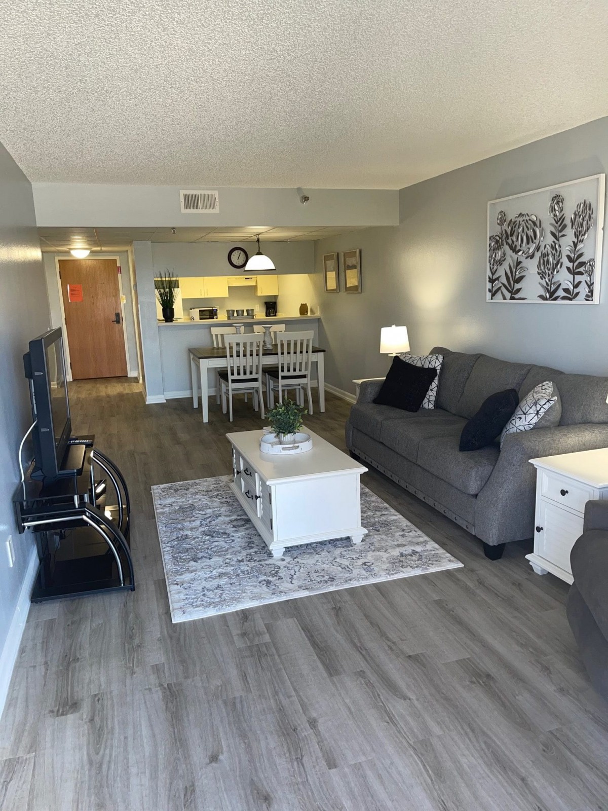 Modern living room with a cozy gray sofa, white coffee table, and a dining area in the background.