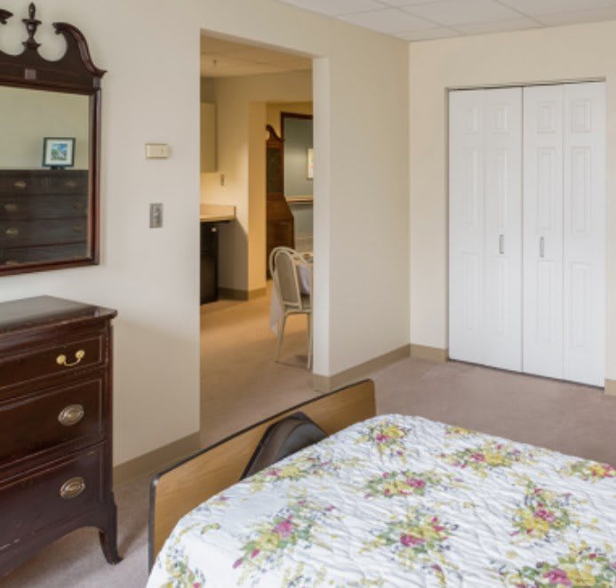 A cozy bedroom with a wooden dresser and mirror, floral bedspread, and white closet doors.