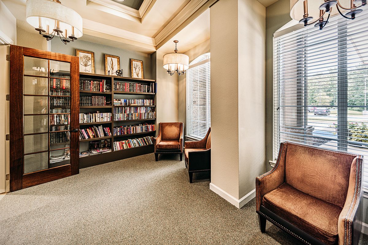 A cozy library corner featuring bookshelves filled with books, comfortable armchairs, and large windows allowing natural light.