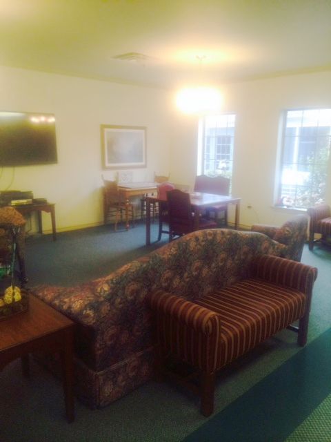 A cozy living room with a variety of seating options and a television, featuring large windows and carpeted flooring.