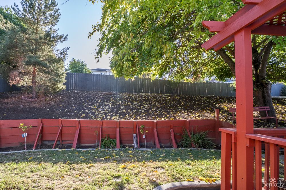 A backyard with a red fence, green grass, and tree offering shade.