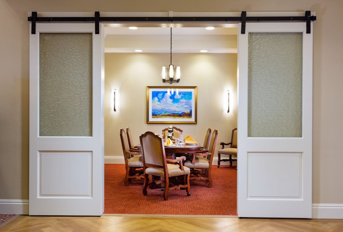 A well-decorated dining room with a table and chairs, illuminated by a chandelier and complemented by artwork on the wall.
