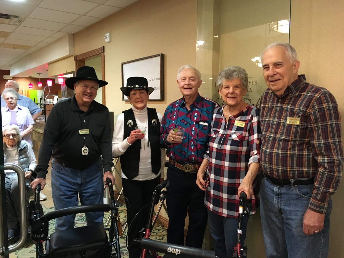 A group of seniors enjoying a social gathering indoors, dressed in casual clothing with some wearing hats and smiling for the camera.